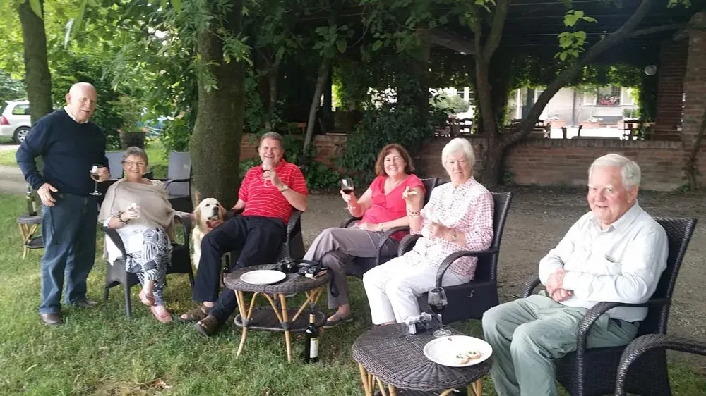 Group relaxing with wine in a shaded garden, dog sitting beside them.