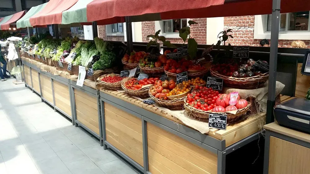 Fresh produce market stand with colorful vegetables in baskets, neatly arranged under red-and-green canopies.