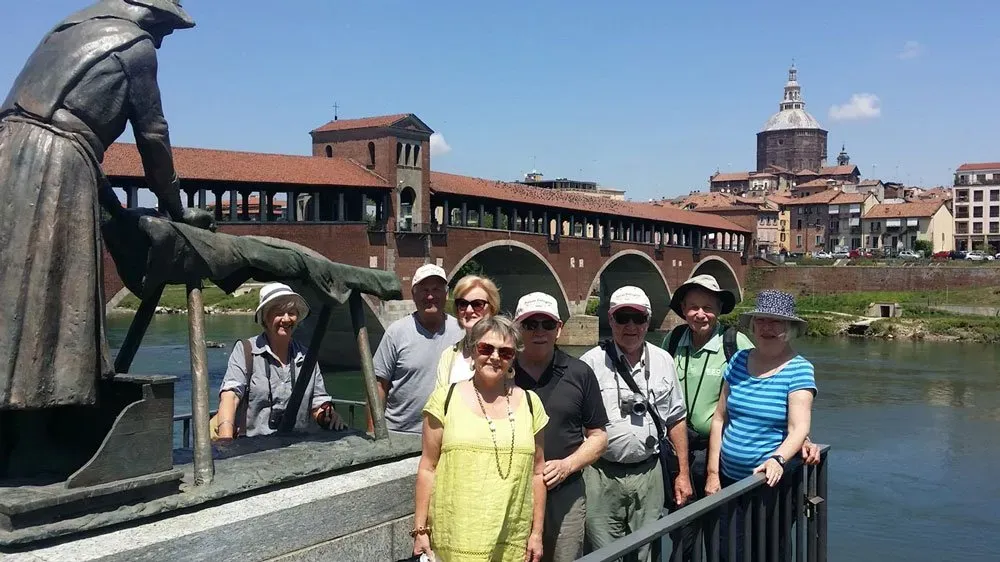 Tour group posing near the statue by Ponte Coperto in Pavia, with the Duomo in clear view behind.