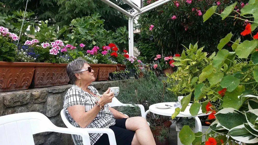 Woman relaxing with coffee in a lush garden surrounded by colorful flowers.