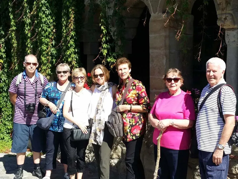 Tour group posing in front of a vine-covered stone building on a sunny day.