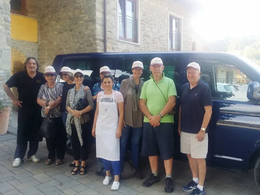 Group of tourists posing in front of a dark van outside a stone building.