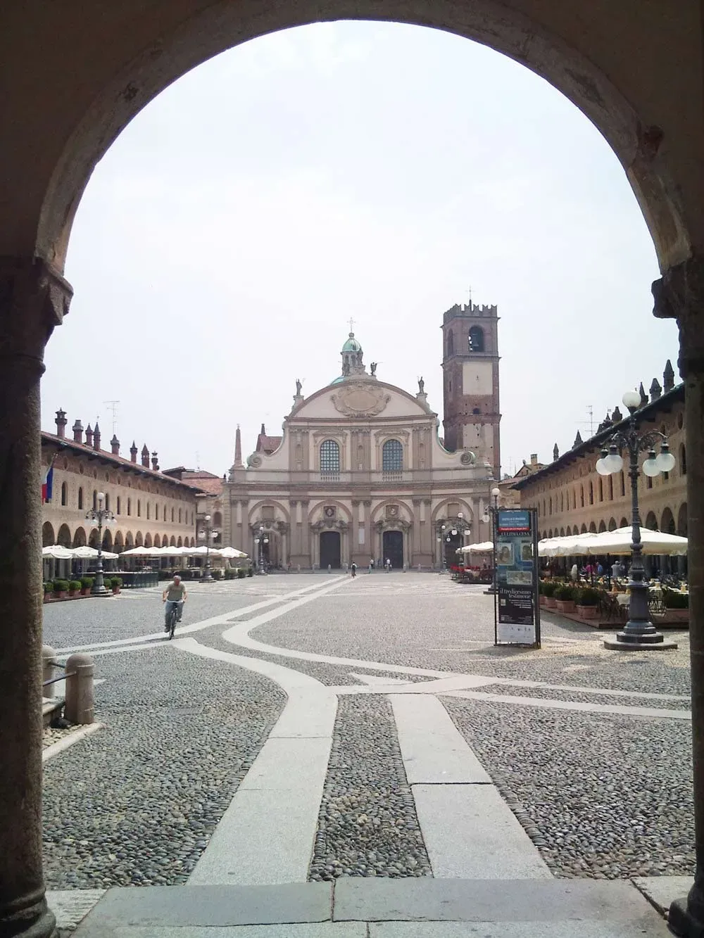 Framed view of Piazza Ducale and the Cathedral of Vigevano through a stone arch.