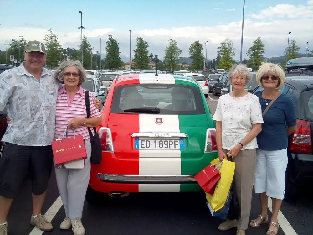 Group posing behind a Fiat 500 painted with the Italian flag in a parking lot.