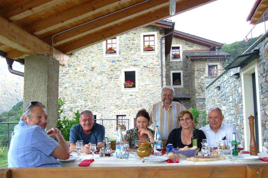 Group having lunch under a covered patio with a stone house and mountain view in the background.