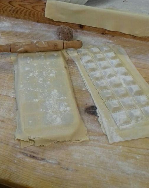 Fresh ravioli being made with dough, a rolling pin, and a ravioli mold on a floured surface.