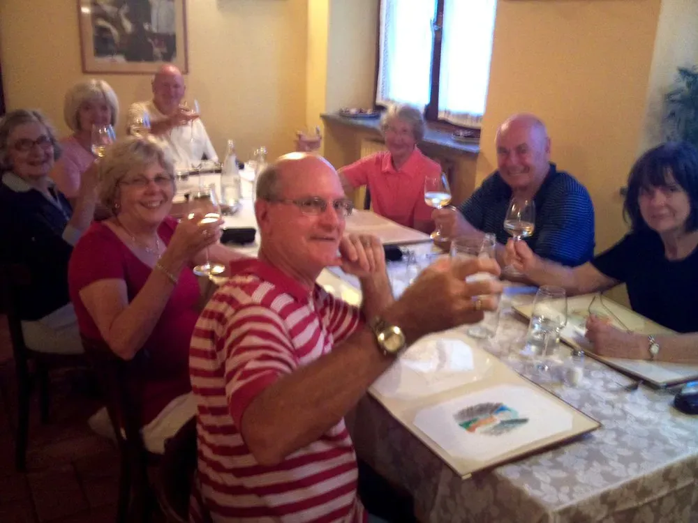 Group of people raising wine glasses while seated around a dinner table in a warmly lit restaurant.