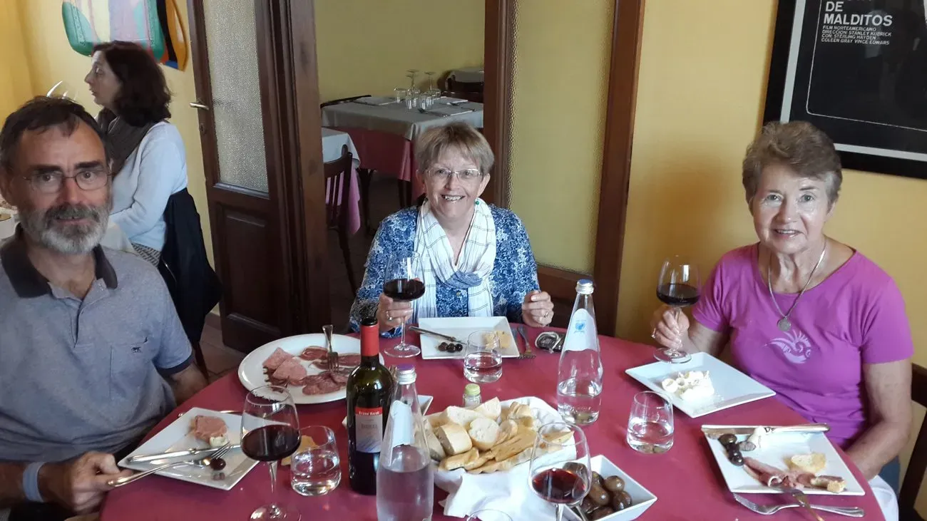 Three people enjoying wine, bread, meats, and cheese at a relaxed indoor lunch.