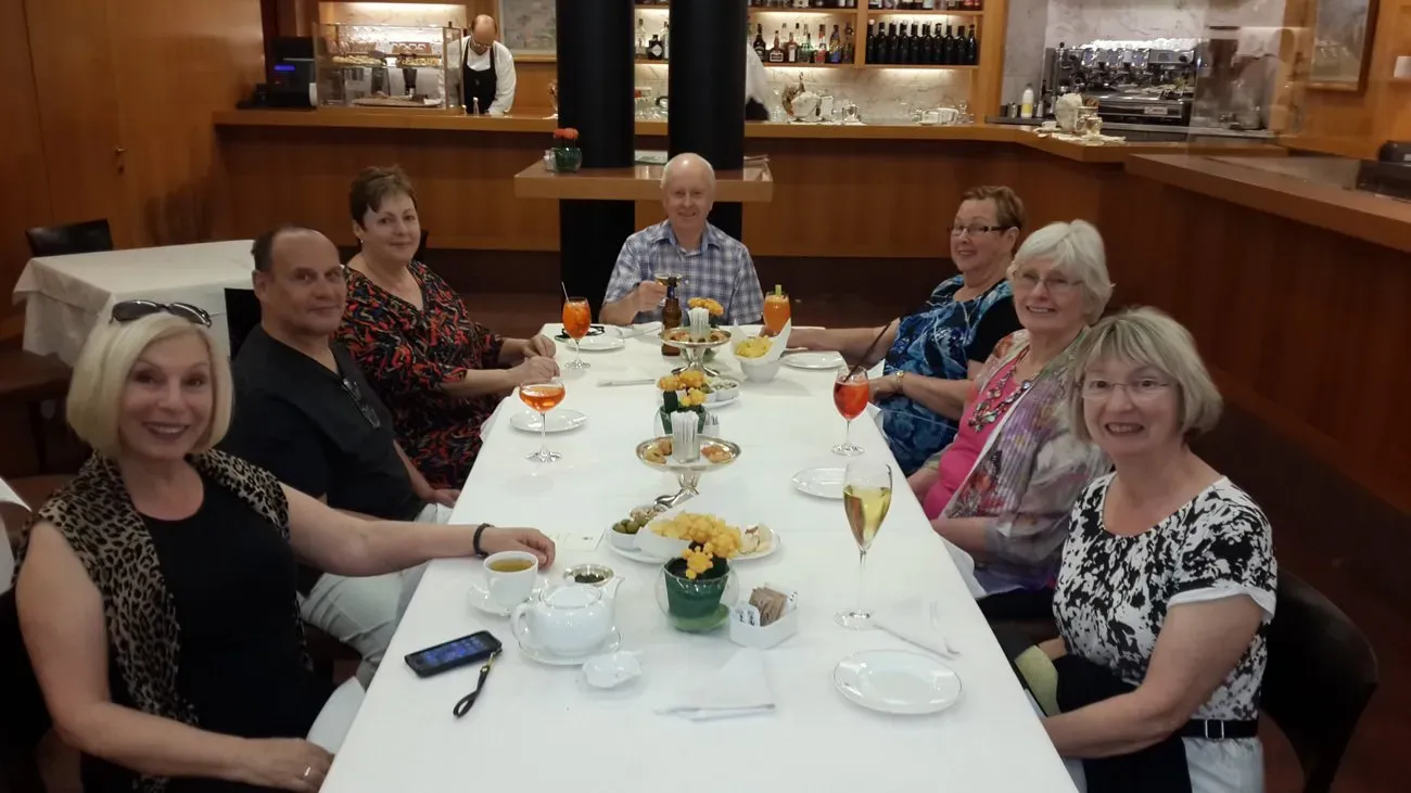 Group of people seated at a long table in a restaurant, enjoying drinks and snacks.