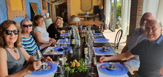 A group of people are sitting at a long table with plates and glasses of wine.