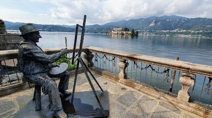 A statue of a man sitting on a chair painting a picture of a lake.