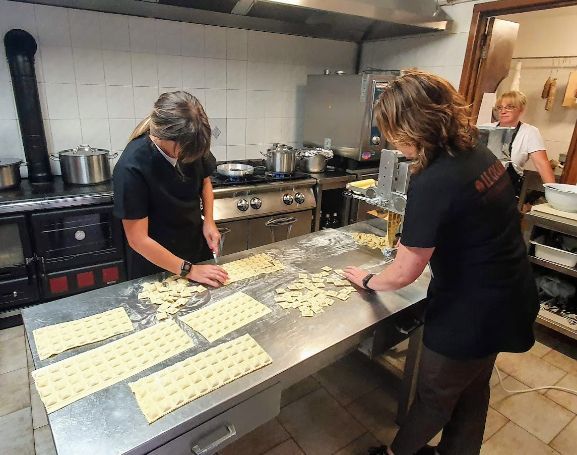 Two women are preparing food in a kitchen and one is wearing a shirt that says ' a ' on it
