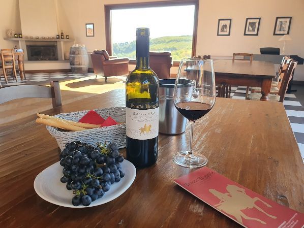 A bottle of wine sits on a wooden table next to a plate of grapes and a glass of wine