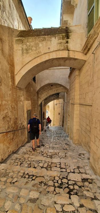 A man is walking down a cobblestone street under an archway.