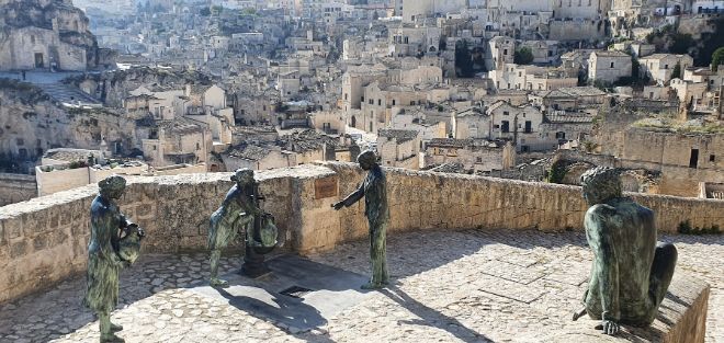 A group of statues are standing on top of a stone wall overlooking a city.