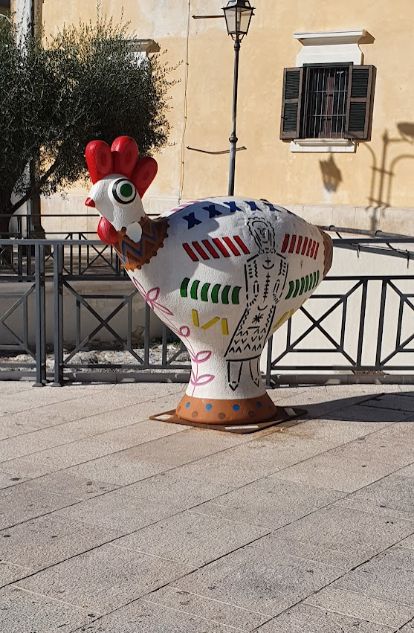 A statue of a rooster with a red crest is sitting on a sidewalk in front of a building