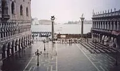 Wet stone plaza flanked by arcaded palaces, leading to two tall columns by the water.