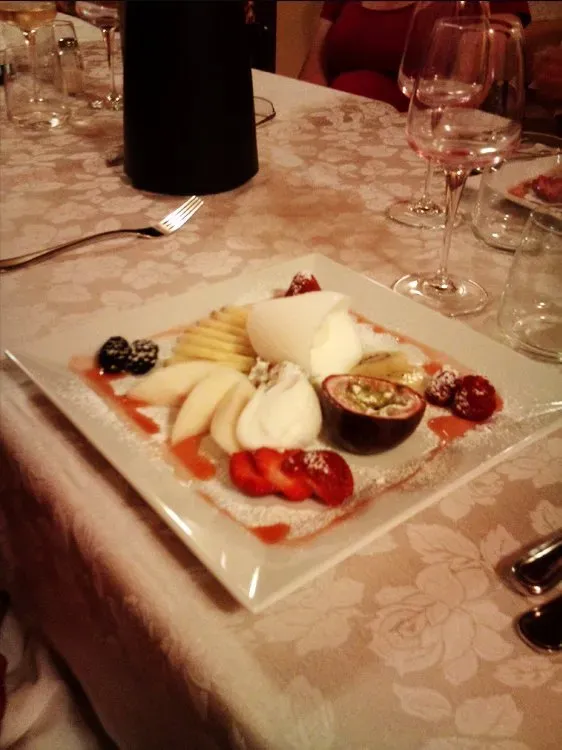 Plate of fresh fruit and sorbet served on a white tablecloth with wine glasses in the background.