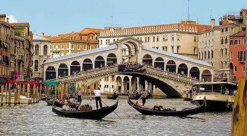 Stone arch bridge lined with shops, gondolas gliding through the Grand Canal below.