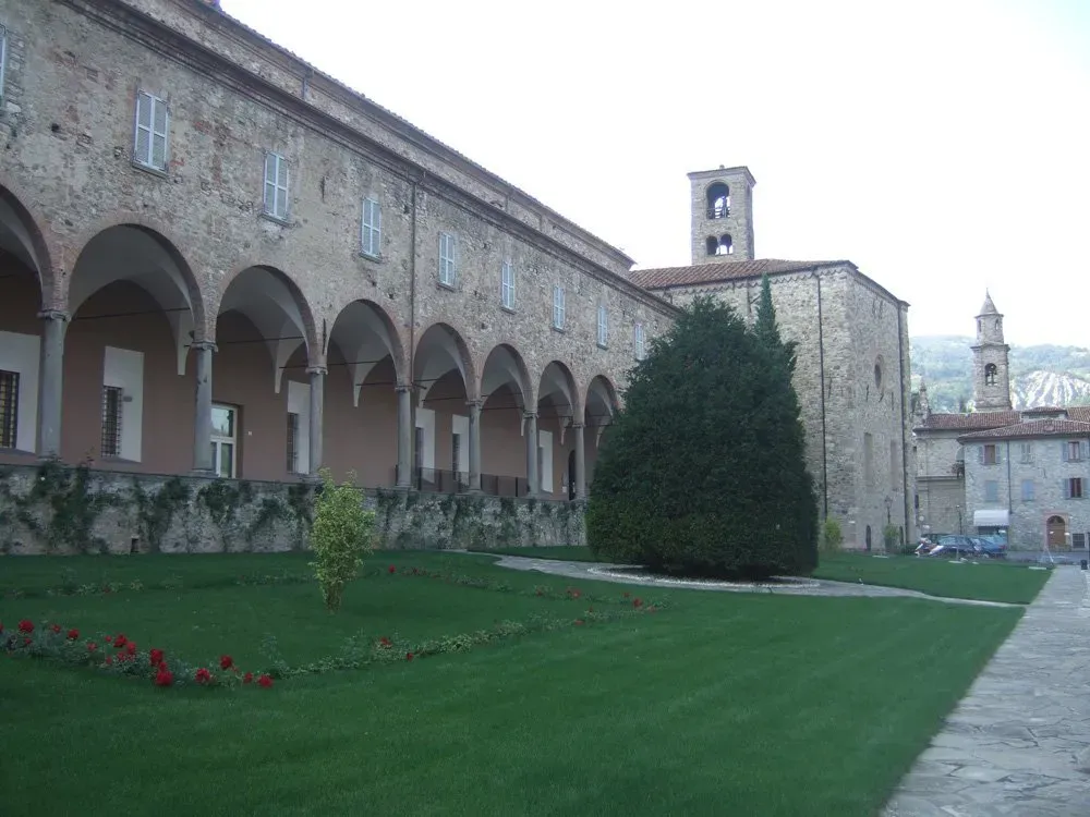 Monastery of Bobbio with arched cloisters, a bell tower, and a manicured garden.