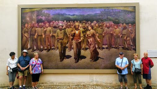 A group of people are standing in front of a large painting.