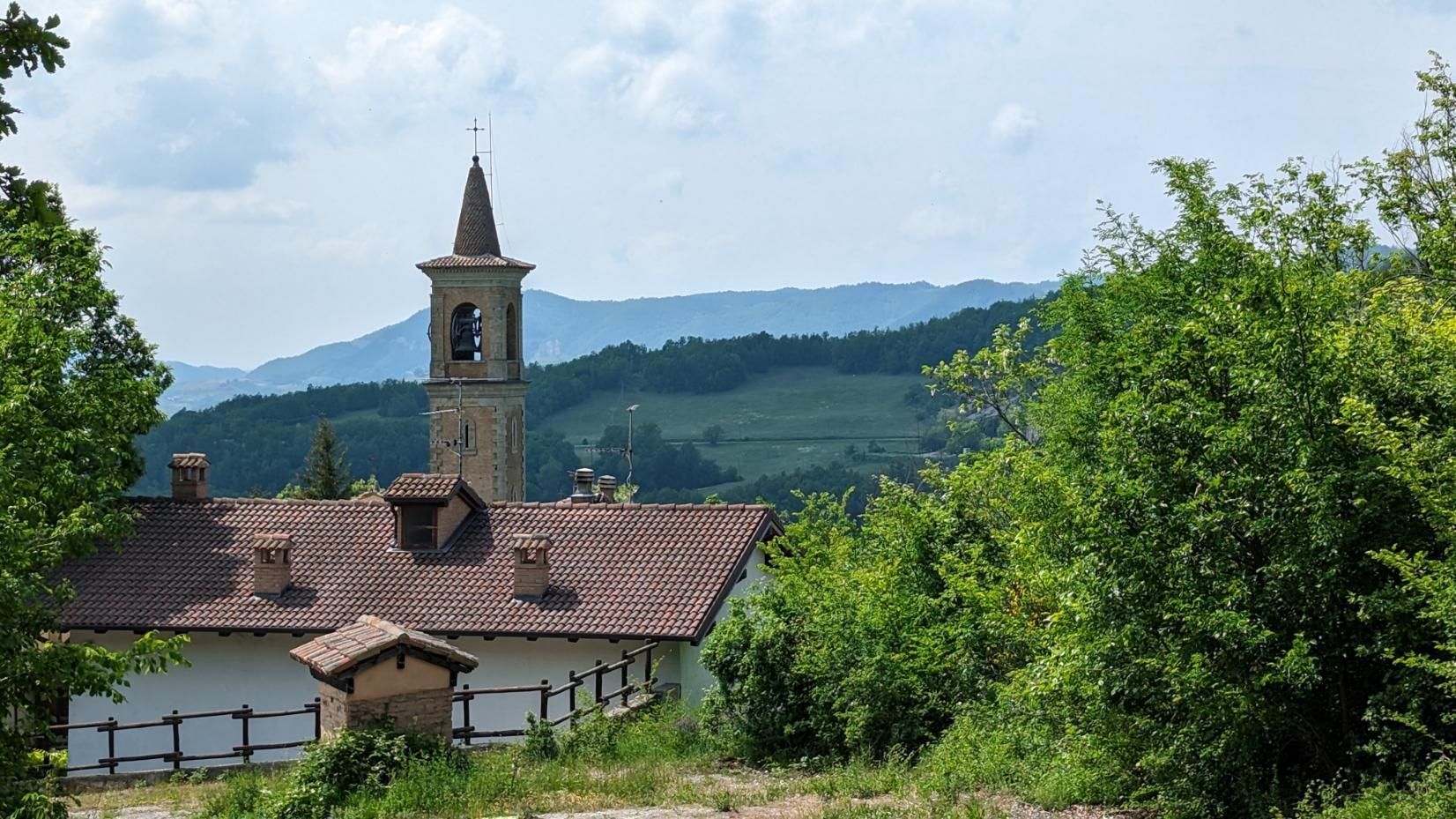 A church tower is surrounded by trees and mountains in the background