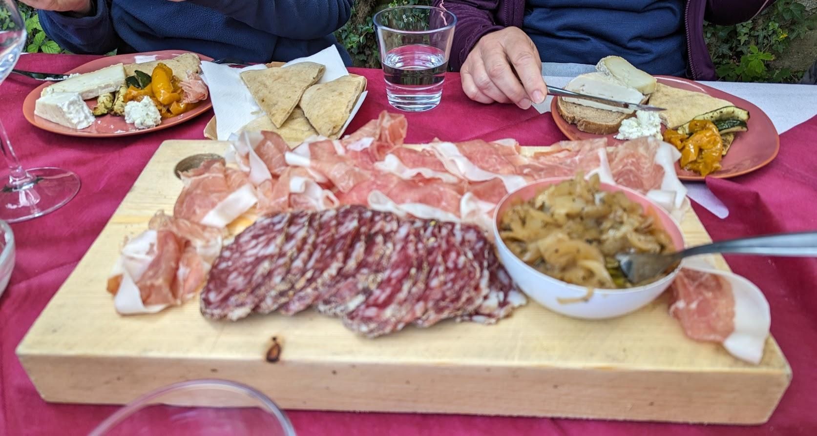 A wooden cutting board topped with meat and a bowl of soup on a table.