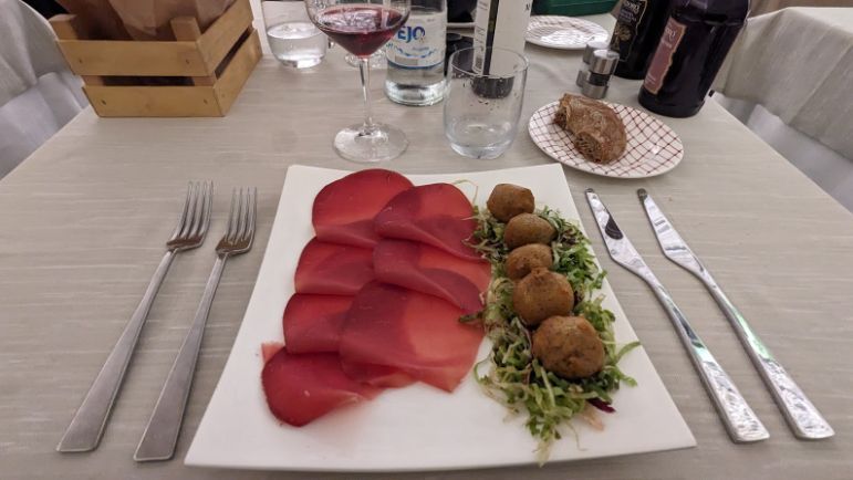 A white plate topped with meat and vegetables on a table with silverware.