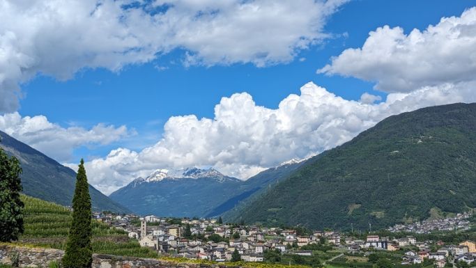 A small town is surrounded by mountains and clouds on a sunny day.