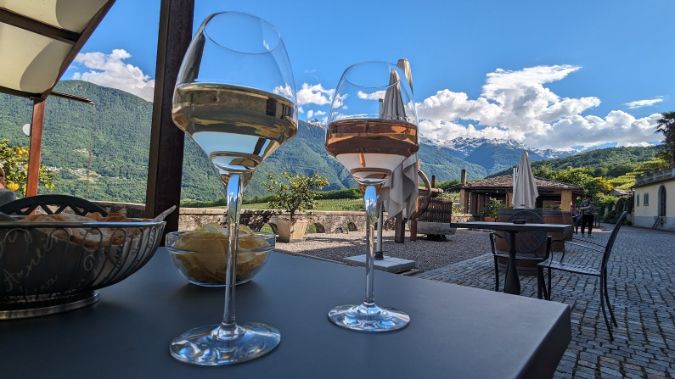 Two glasses of wine are sitting on a table with mountains in the background.