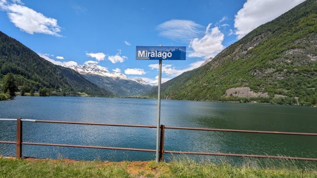 A sign for miralago is sitting next to a lake surrounded by mountains.