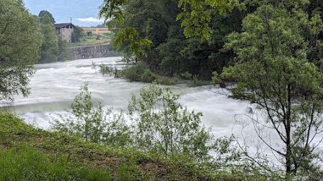 A river surrounded by trees and grass with a bridge in the background.