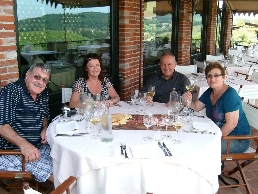 A group of four people enjoy wine and antipasti on a terrace with vineyard views.