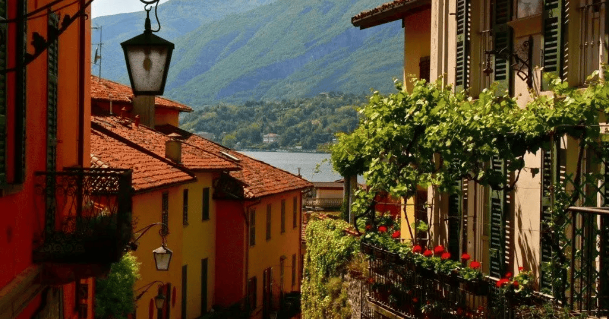 Narrow alley with red-tiled rooftops, lake view, and mountain backdrop in Lake Como.