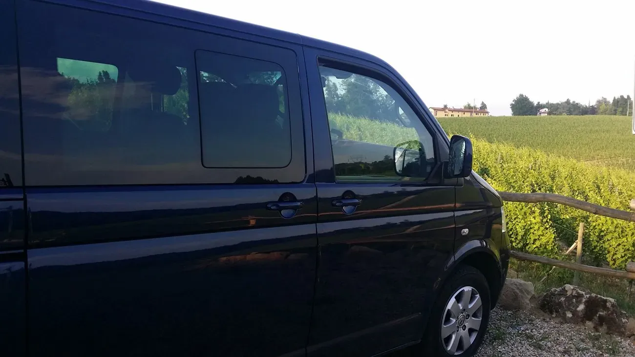 A black van parked beside a vineyard, with rolling hills and farmhouses in the background.
