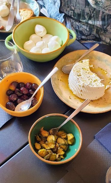 A table topped with bowls of food including a slice of cheese and olives.