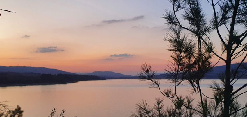 A sunset over a lake with trees in the foreground and mountains in the background.