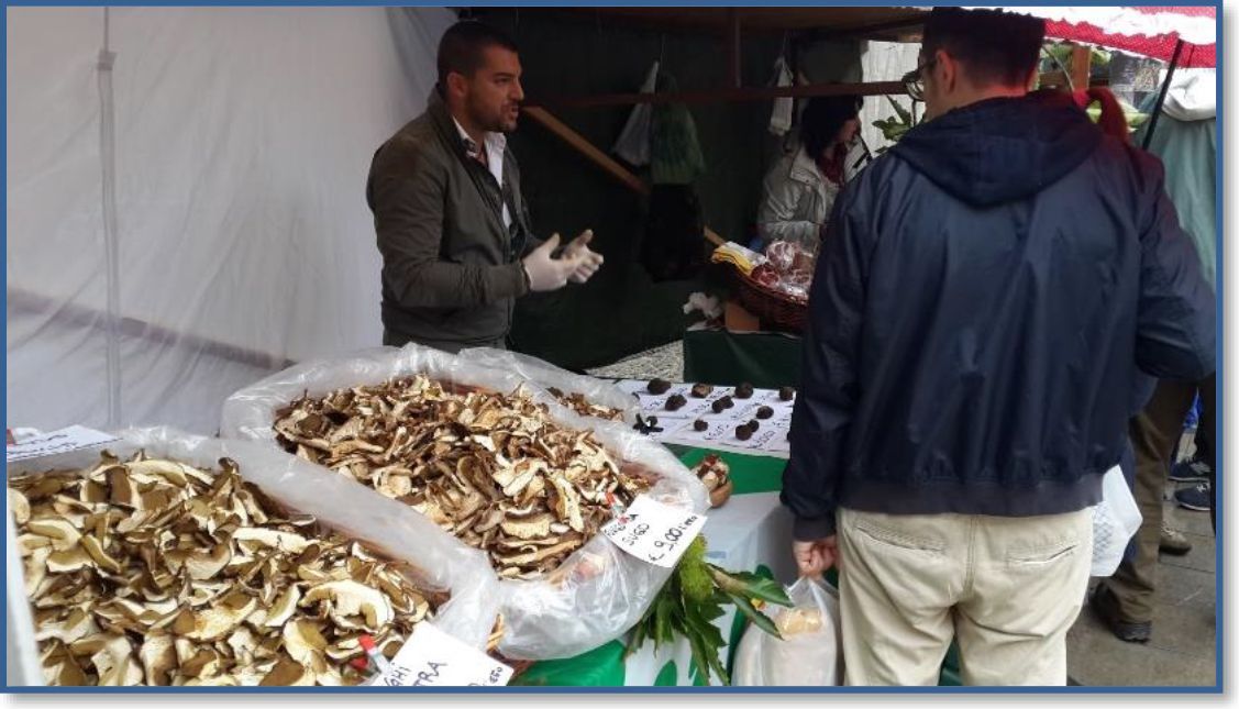 A man is standing in front of a pile of mushrooms