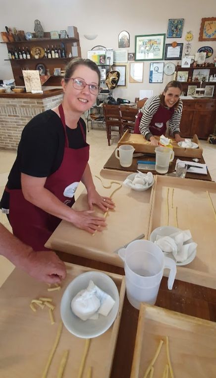 Two women are sitting at a table making pasta.