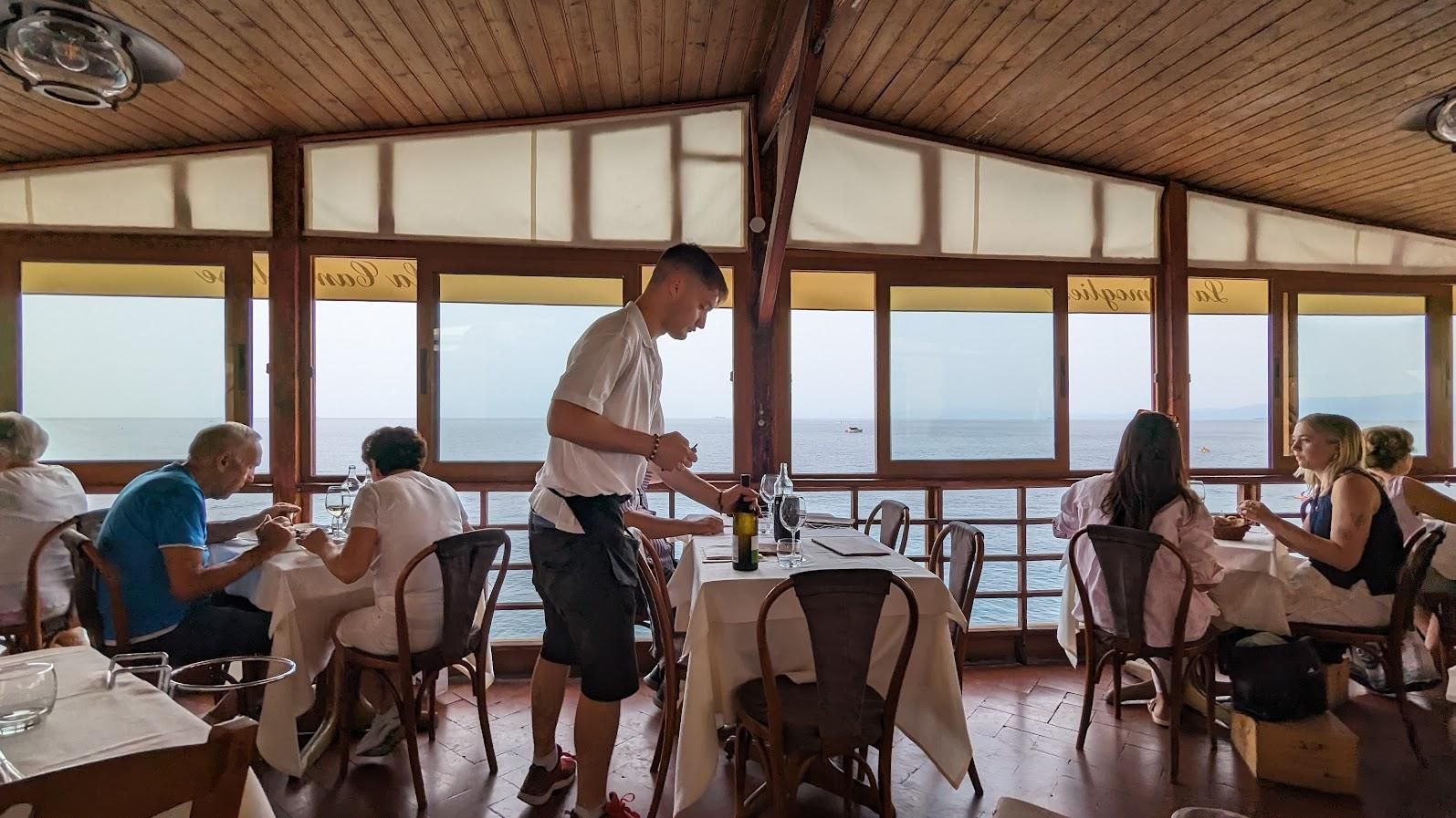 A group of people are sitting at tables in a restaurant with a view of the ocean.