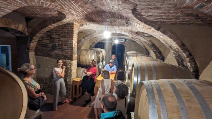 A group of people are standing around barrels in a wine cellar.