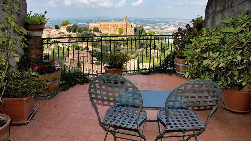 Terracotta patio with metal chairs and potted plants overlooking the rooftops and countryside of Montepulciano, Tuscany.
