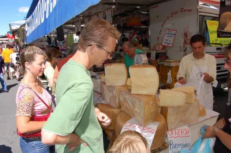 Shoppers browse massive cheese blocks at an open-air Italian market.