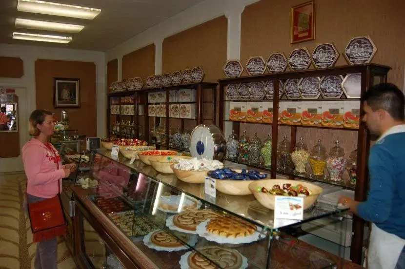 Woman buying sweets at a traditional Italian candy and pastry shop with wooden shelves and glass displays.