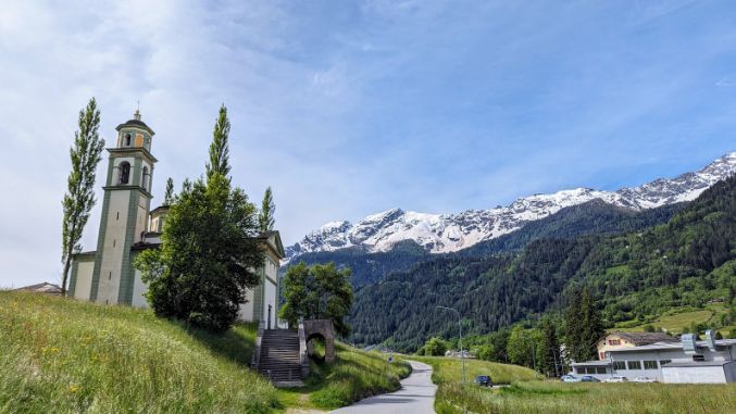 There is a church in the middle of a field with mountains in the background.