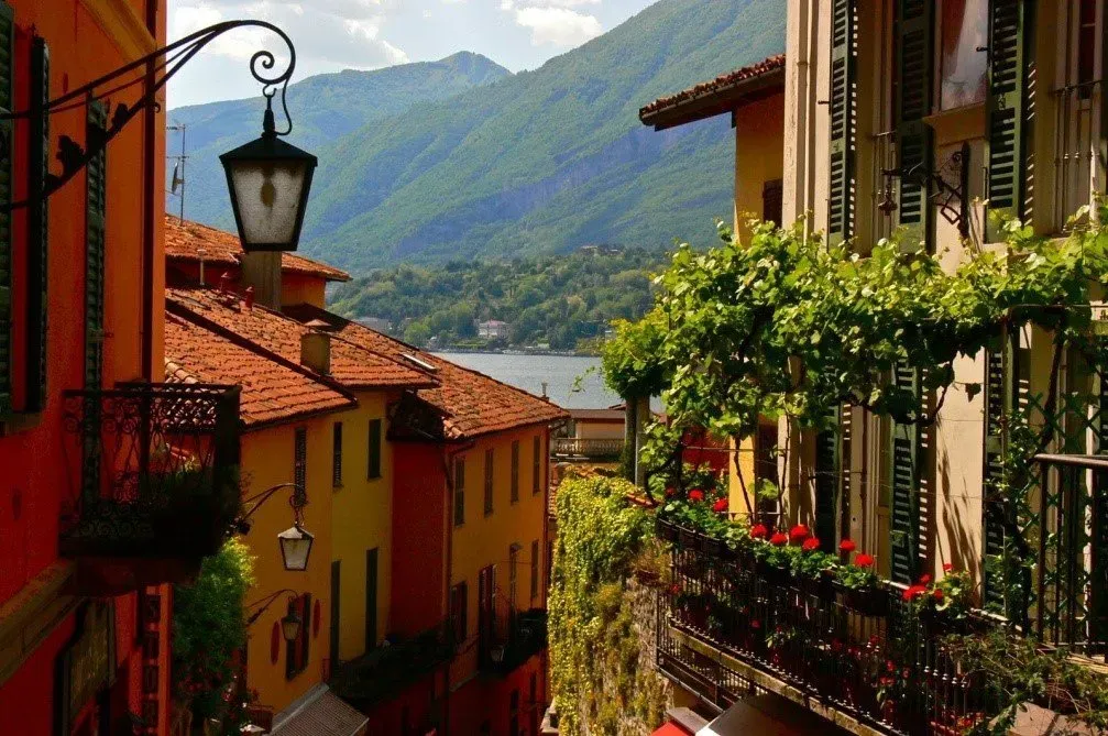 Narrow alley with red-tiled rooftops, lake view, and mountain backdrop in Lake Como.