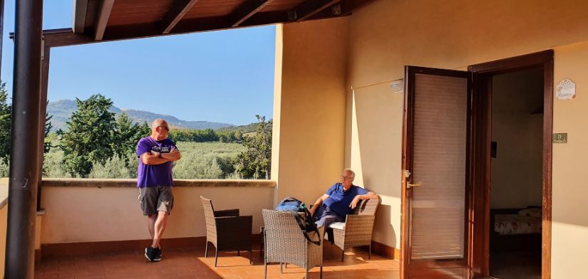 Two men are standing and sitting on a balcony.