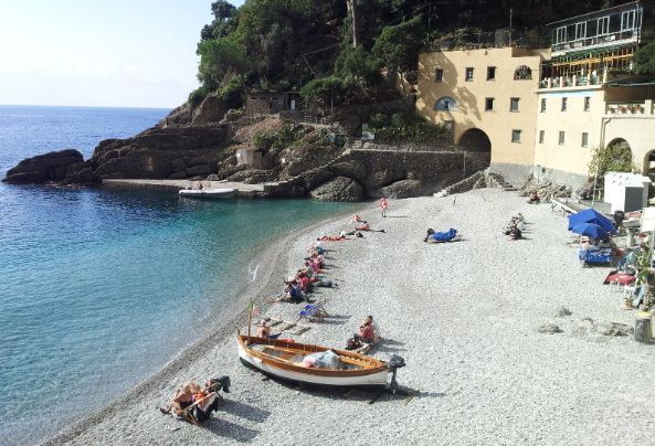 A beach with a boat in the water and a building in the background