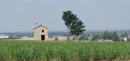 A small stone building is sitting in the middle of a grassy field.
