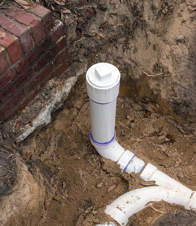 A white pipe is sitting in the dirt next to a brick wall.